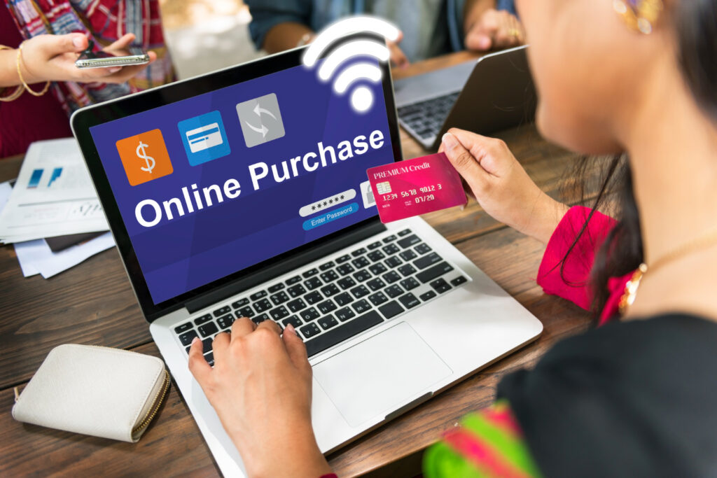 A woman using a laptop for an online purchase, holding a credit card, with a login screen visible on the computer.