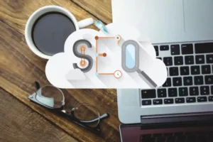 A cup of coffee, eyeglasses, and a laptop with an "SEO" graphic on a wooden desk, symbolizing digital marketing strategies.