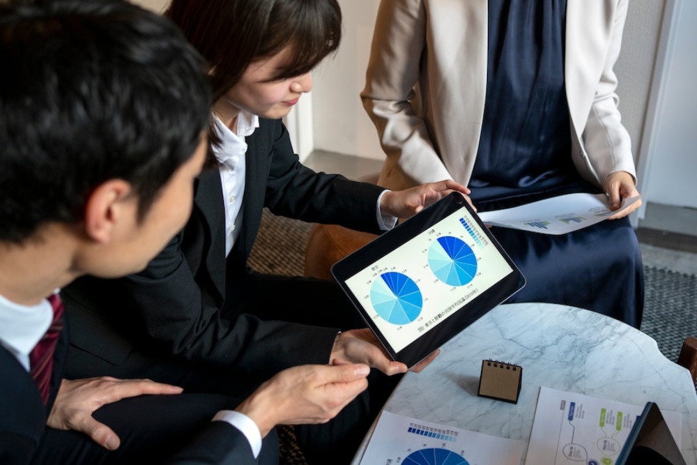  Business professionals analyse pie charts on a tablet in a meeting.