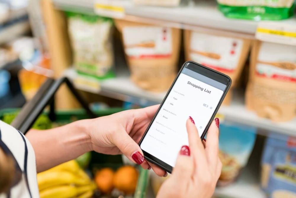 Person using a smartphone to check a digital shopping list in a grocery store aisle.