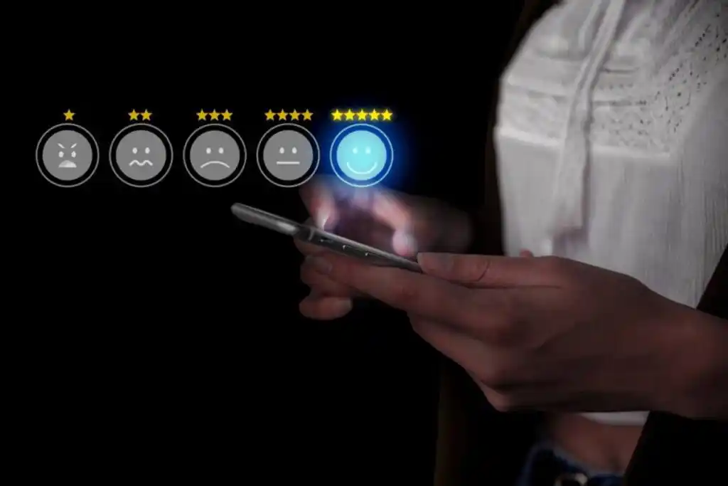 A person rates their experience on a mobile device, selecting a smiling emoji among various emotion icons on a dark background.