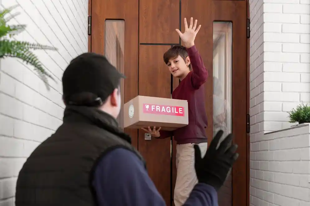 A child stands at the door, holding a fragile package, while a person in a black vest gestures from the porch.