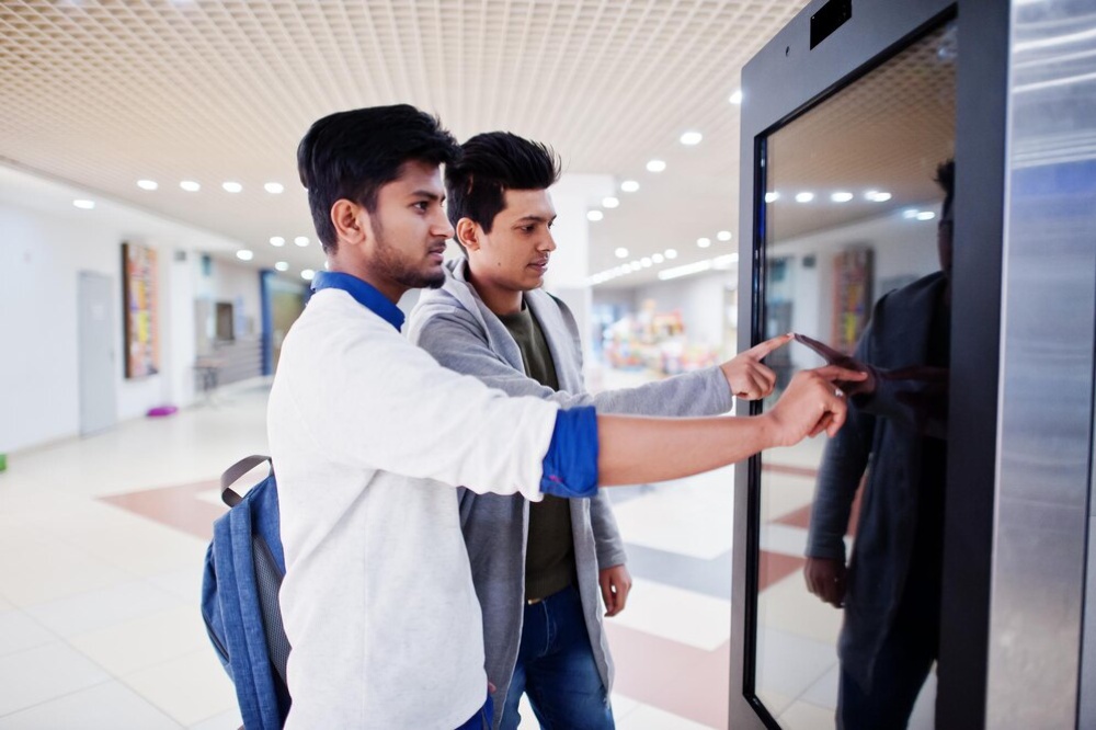 Two young men interacting with a digital information screen in a modern indoor setting. 