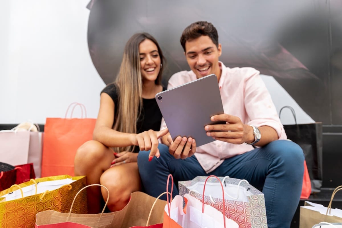 Young man and woman happily looking at a tablet surrounded by shopping bags.